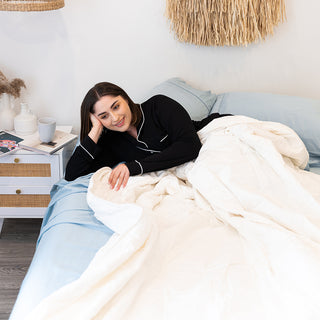A woman luxuriously rests on a bed adorned with plush pillows. Experience the epitome of comfort with the 4 Seasons Goose Down Quilt, your key to tranquil and revitalizing sleep all year round.