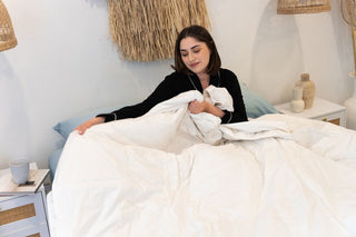 women in bed holding bed quilt in hand on top of her while looking down