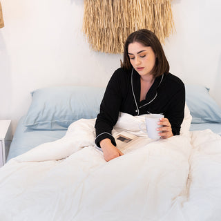 Women in bed with her warm winter duck doona reading a book and drinking tea