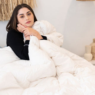 woman sitting on a bed covered with Sienna Living Luxury Goose Feather Down Quilt.